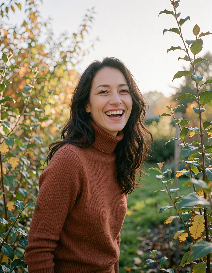 Woman with long dark hair in a rust turtleneck laughing in a garden, picturing a happy first week of online dating